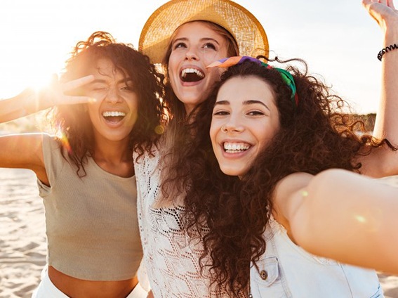 Group of three young women smiling in the sun while taking a selfie